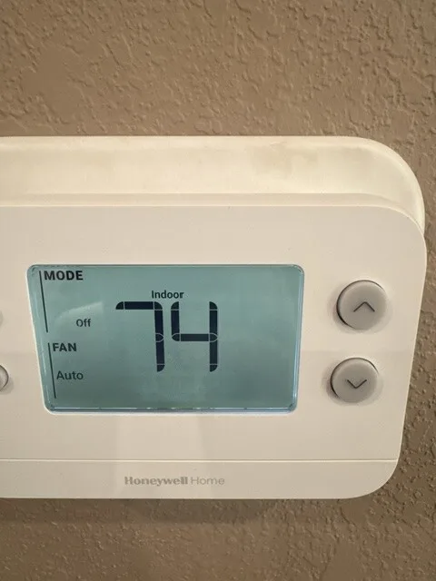 Digital thermostat installed on a wall, reading 74 degrees indoors